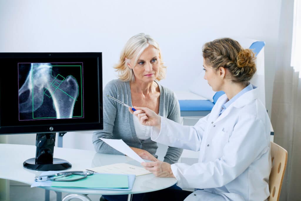 A female doctor is pointing at an X-ray and talking to an older female patient about osteoporosis.