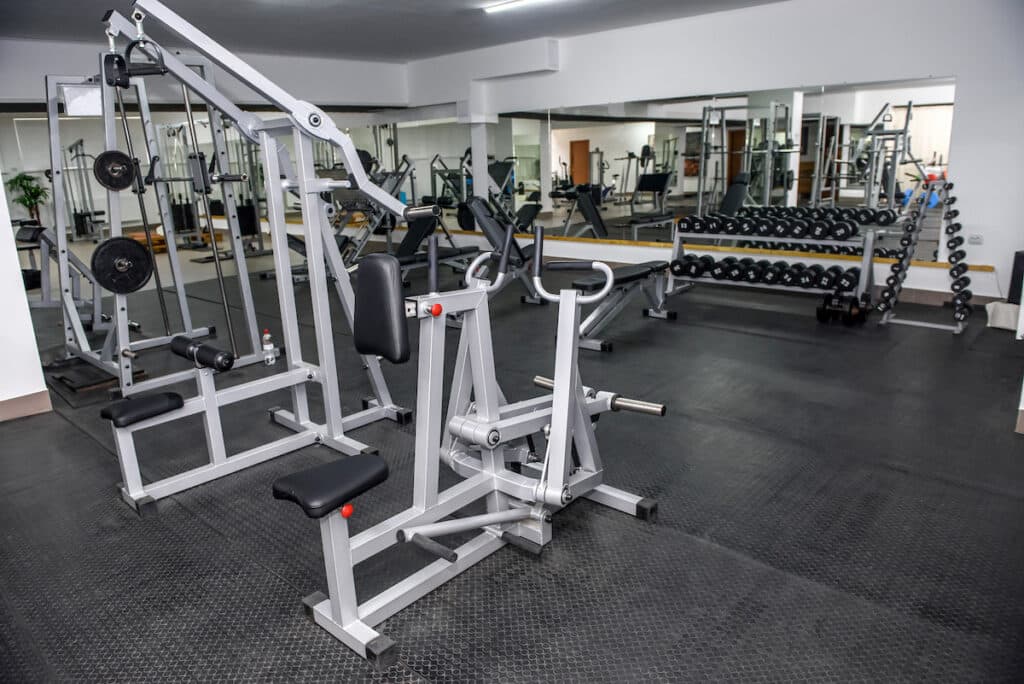 A gym with weight racks and other workout equipment lining the walls and positioned in the middle of the room. The walls have mirrors.