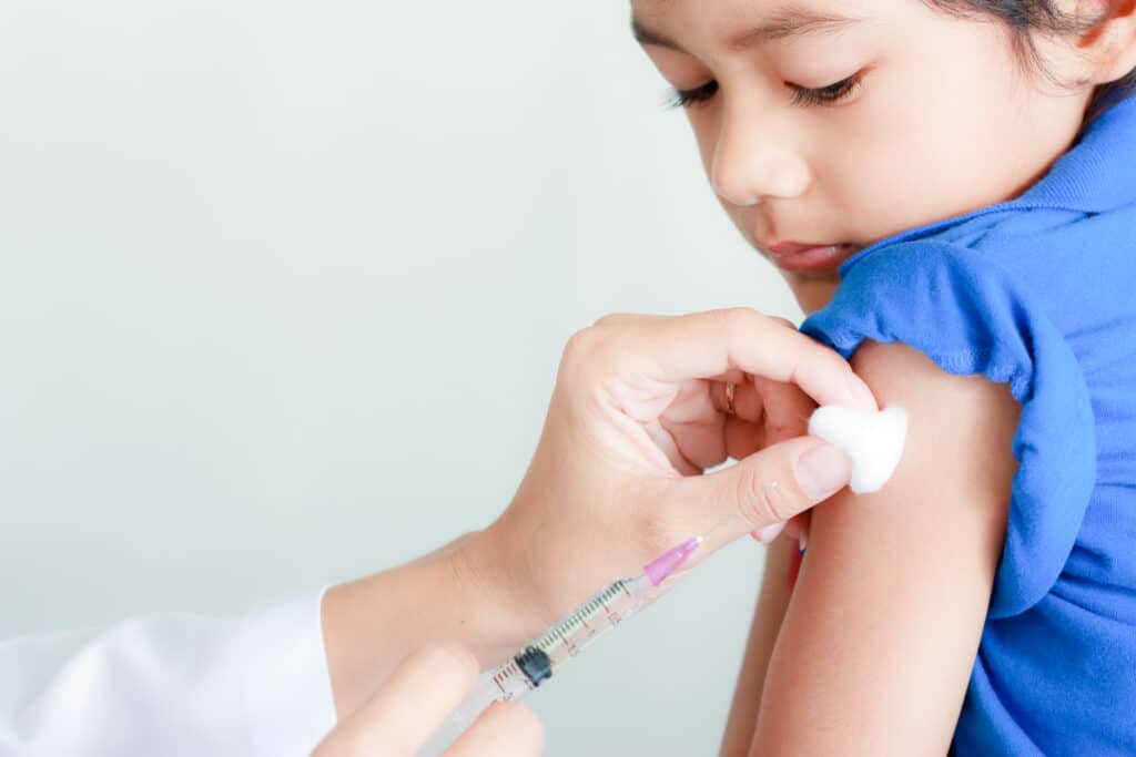 A close-up of a child about to receive an immunization in his left arm.