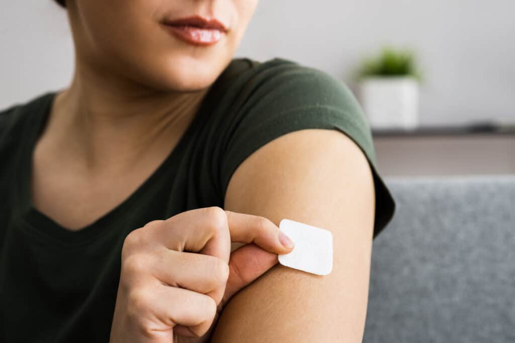 A closeup of a woman placing a nicotine patch on her upper arm.