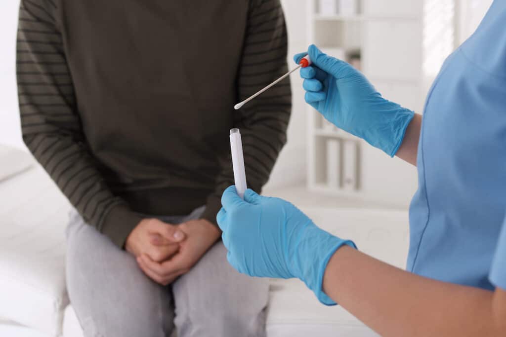 A healthcare professional holds a swab in front of a patient. They are about to perform an STD test.