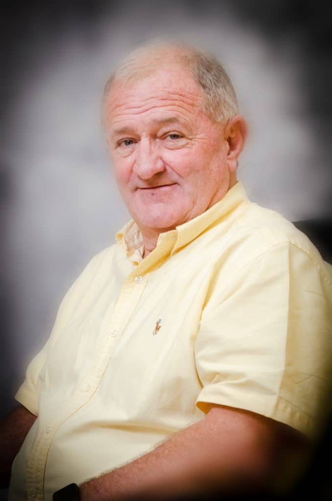 A headshot of Johnny Lockley. He's older, white, with short hair. He's wearing a short-sleeved yellow button-down shirt.