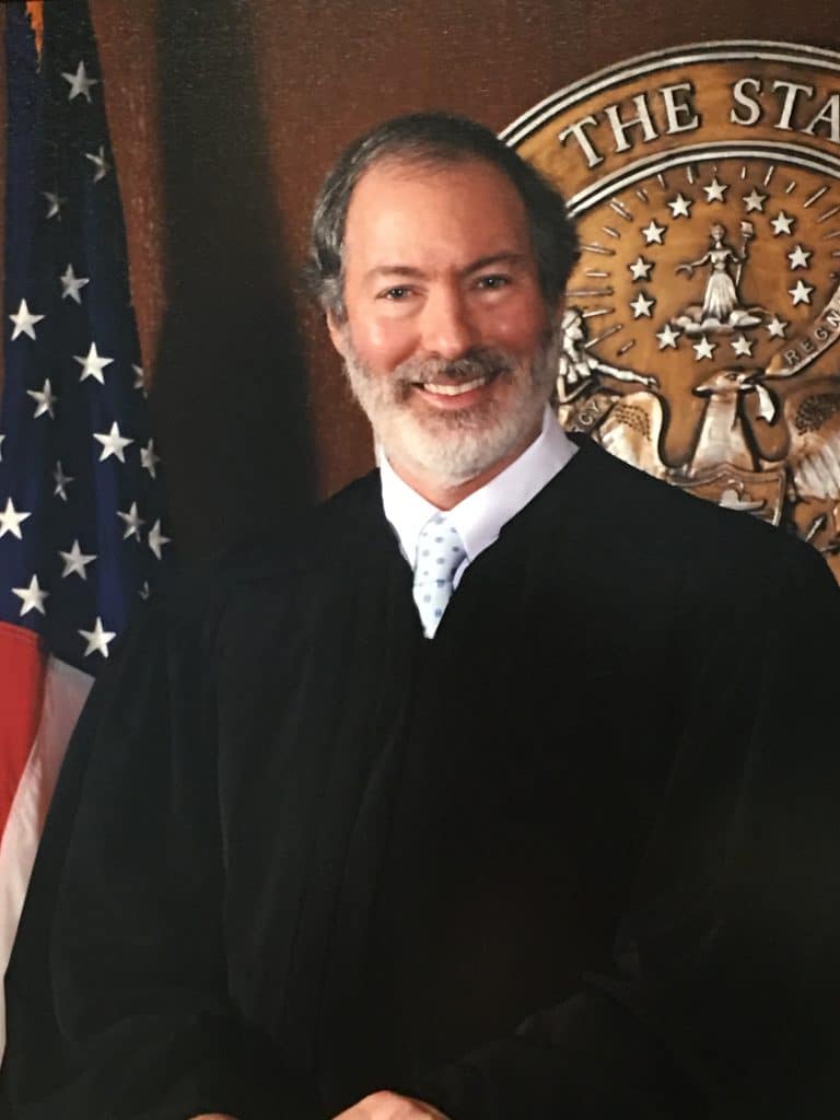 A headshot of Raymond Abramson. He's older, white, and is dressed in his judge's robes. He's in front of an Arkansas Seal.